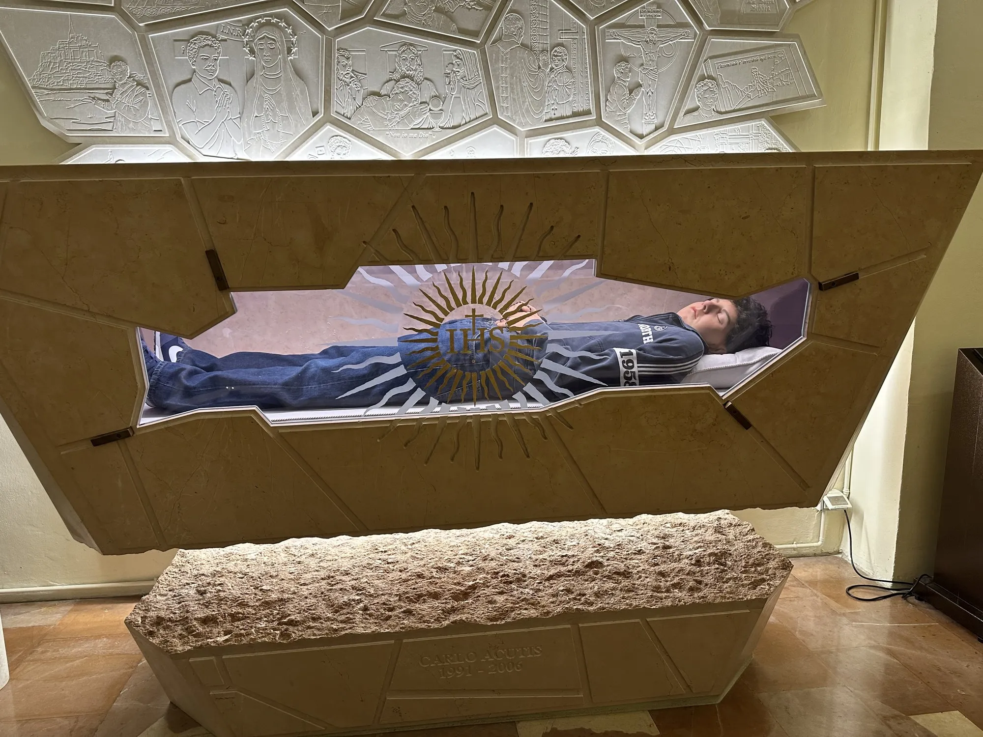 La tomba di Carlo Acutis nel Santuario della Spogliazione, con il sarcofago di pietra e vetro e l’iscrizione 1991-2006